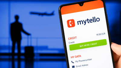 Person holding a smartphone with the mytello app at an airport while a plane departs in the background.